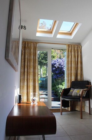 A room with a wooden table, a chair, and a glass of water. There are two skylights above a sliding glass door leading to an outdoor area with plants.