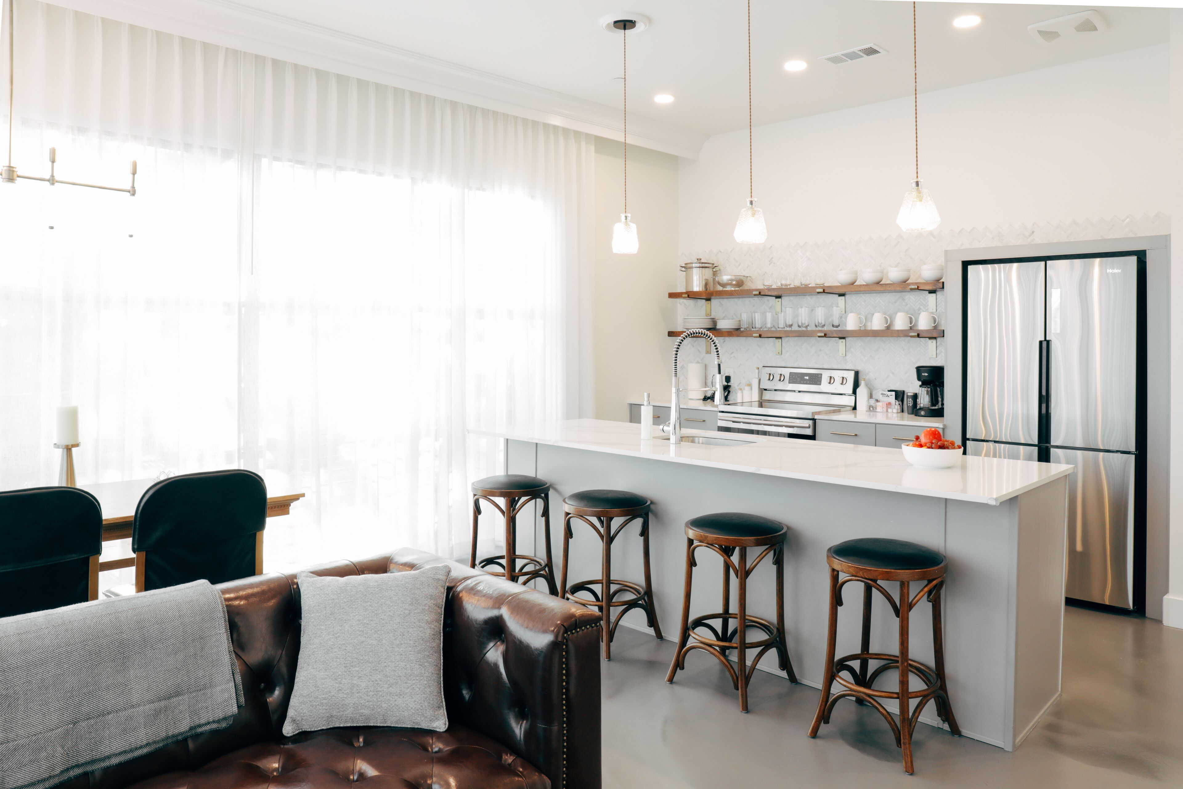A modern kitchen with a central island, bar stools, and a dining area with a leather couch.