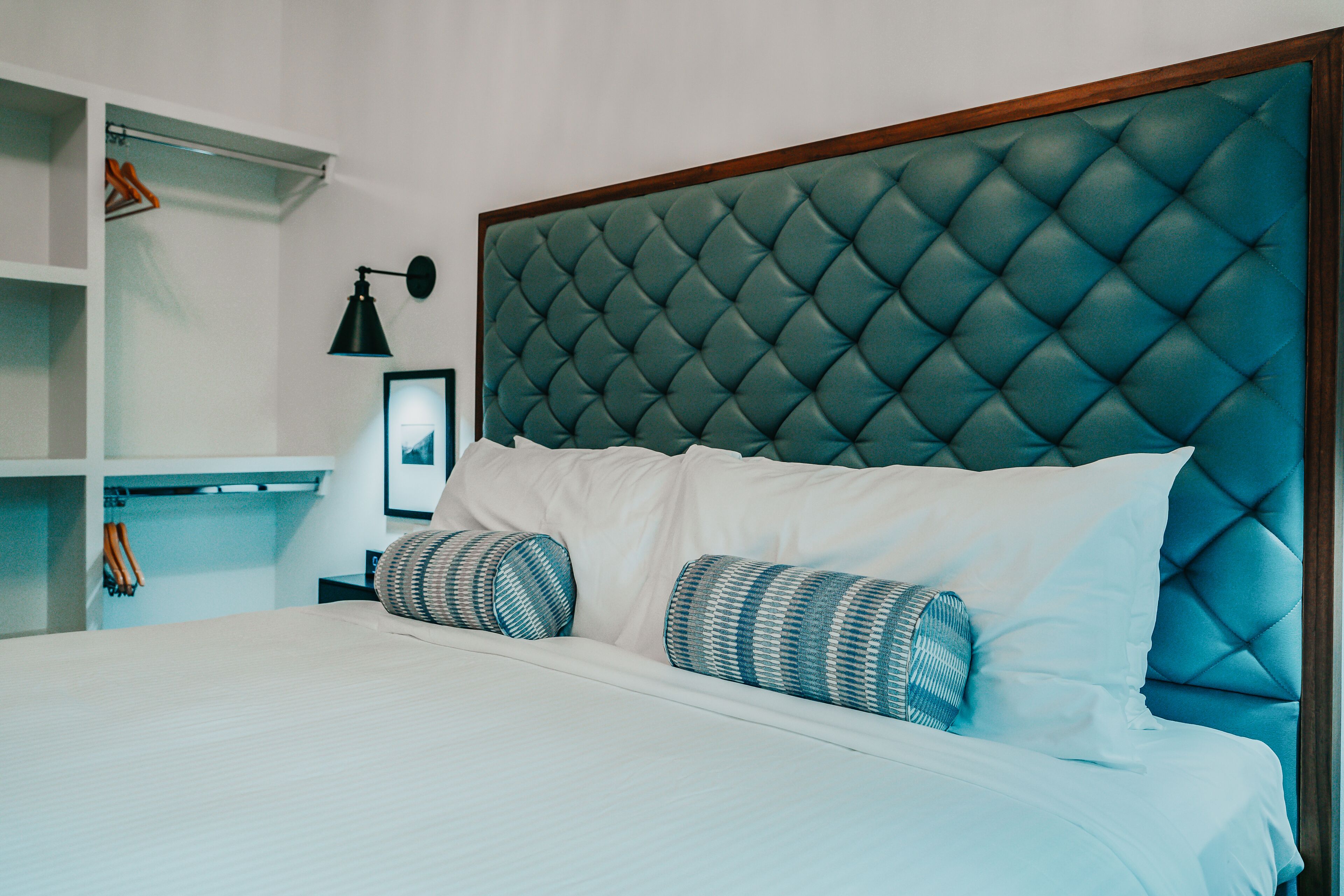 A neatly made bed with a tufted headboard, white bedding, and two patterned pillows.