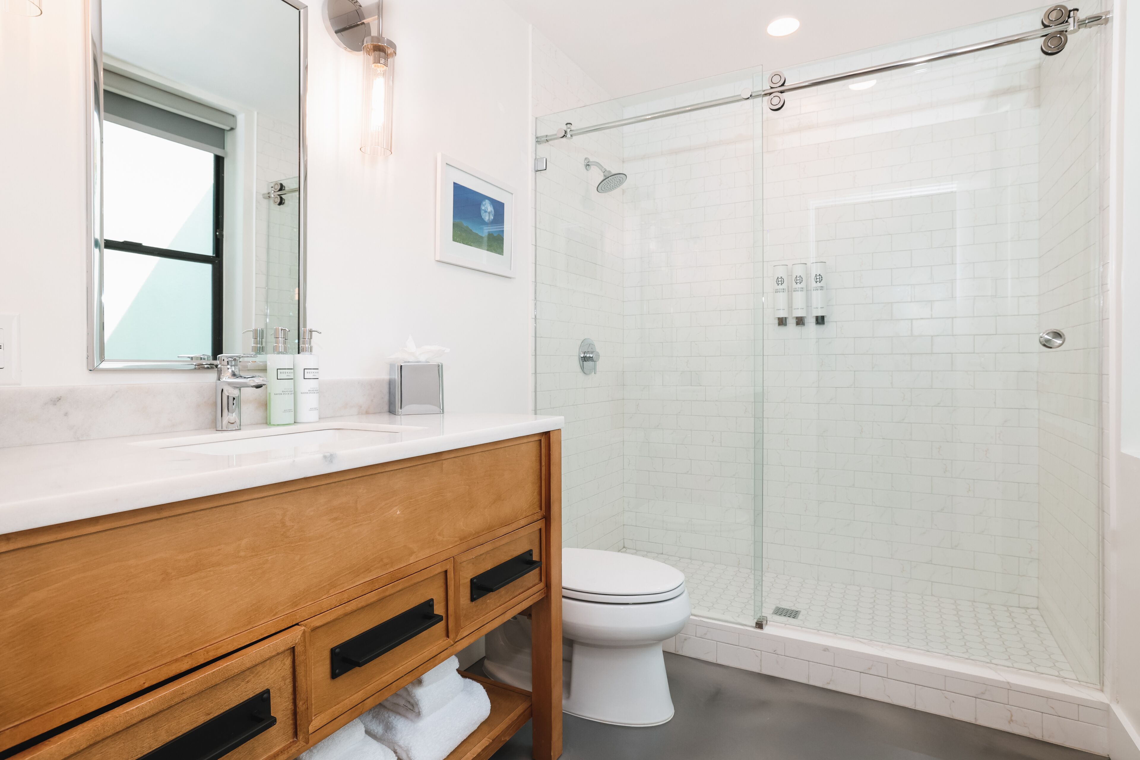 A modern bathroom with a wooden vanity, white toilet, and a glass-enclosed shower area.