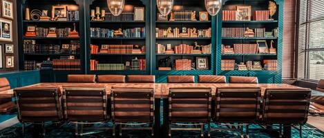A library with bookshelves, a dining table with chairs, and a patterned carpet.