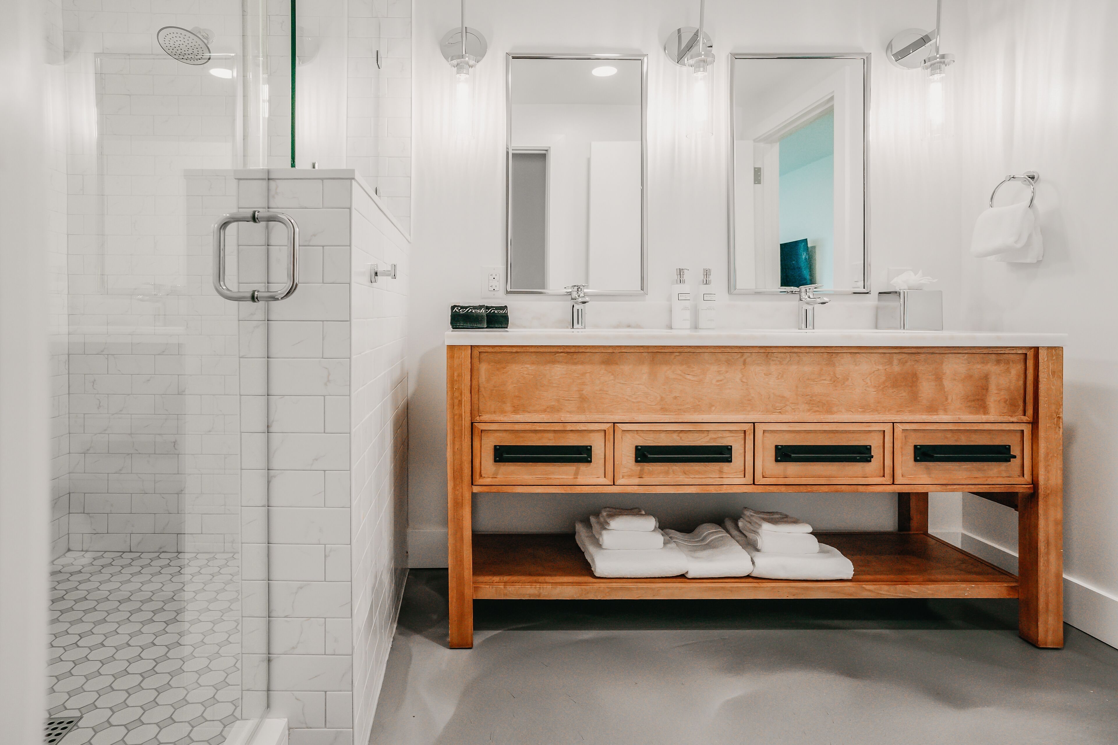 A modern bathroom with a shower, a wooden vanity with drawers, and a large mirror.