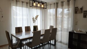 A dining area with a wooden table and chairs, sheer curtains, and a hanging light fixture.
