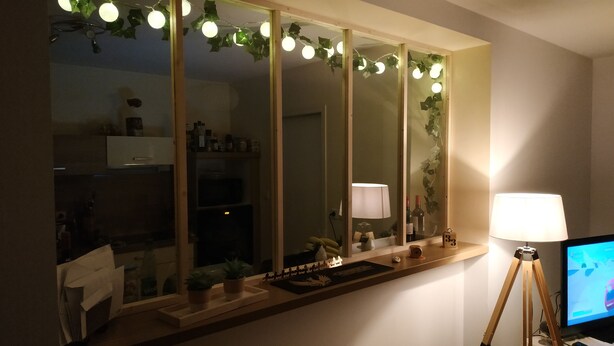 A bathroom with a large mirror, a vanity, a sink, and a toilet. There are plants on the vanity and a lamp on the side.