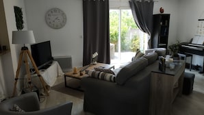 A living room with a sofa, a coffee table, a TV on a tripod, a clock on the wall, and a piano.