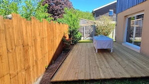 A wooden deck with a covered table, surrounded by a wooden fence and a house with a sliding glass door.