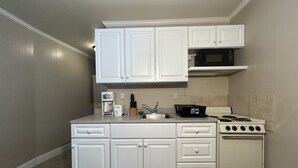 A compact kitchen with white cabinetry, a built-in microwave, a gas stove, and a coffee maker. - Elis Apartments Unit 6 (Ocean City)