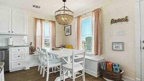 Uma cozinha com armários brancos, uma mesa de jantar com cadeiras, um lustre e vista para a varanda.