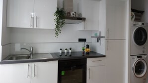 A modern kitchen with white cabinets, a stainless steel sink, a dishwasher, a built-in oven, and a washing machine.