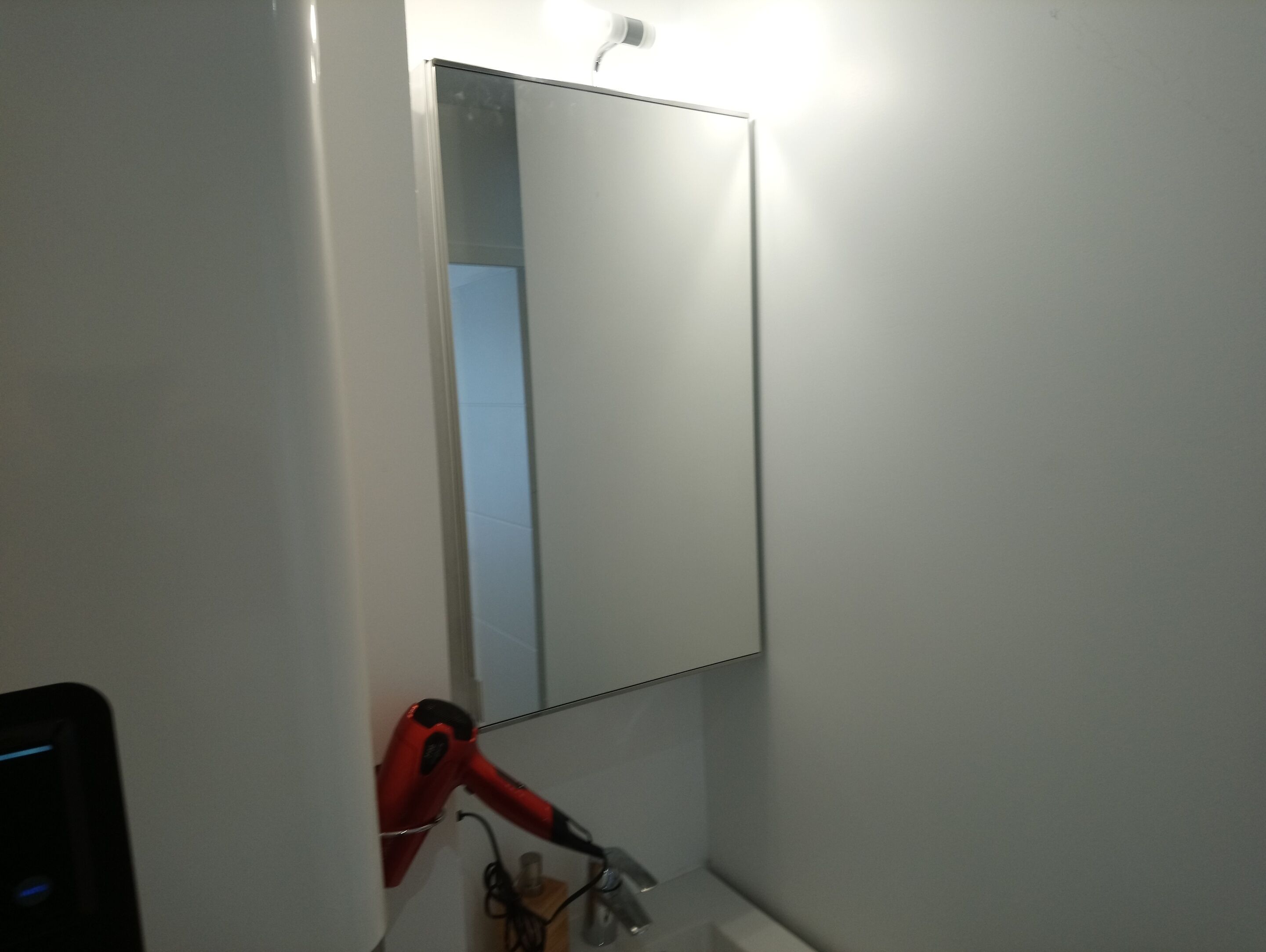 A bathroom with a mirror, a red hairdryer, and a sink.
