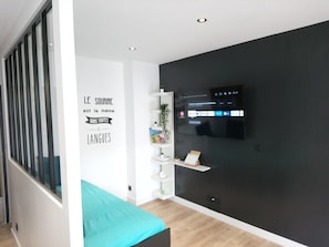 Una habitación moderna con cama, televisión instalada en la pared y una frase motivacional.