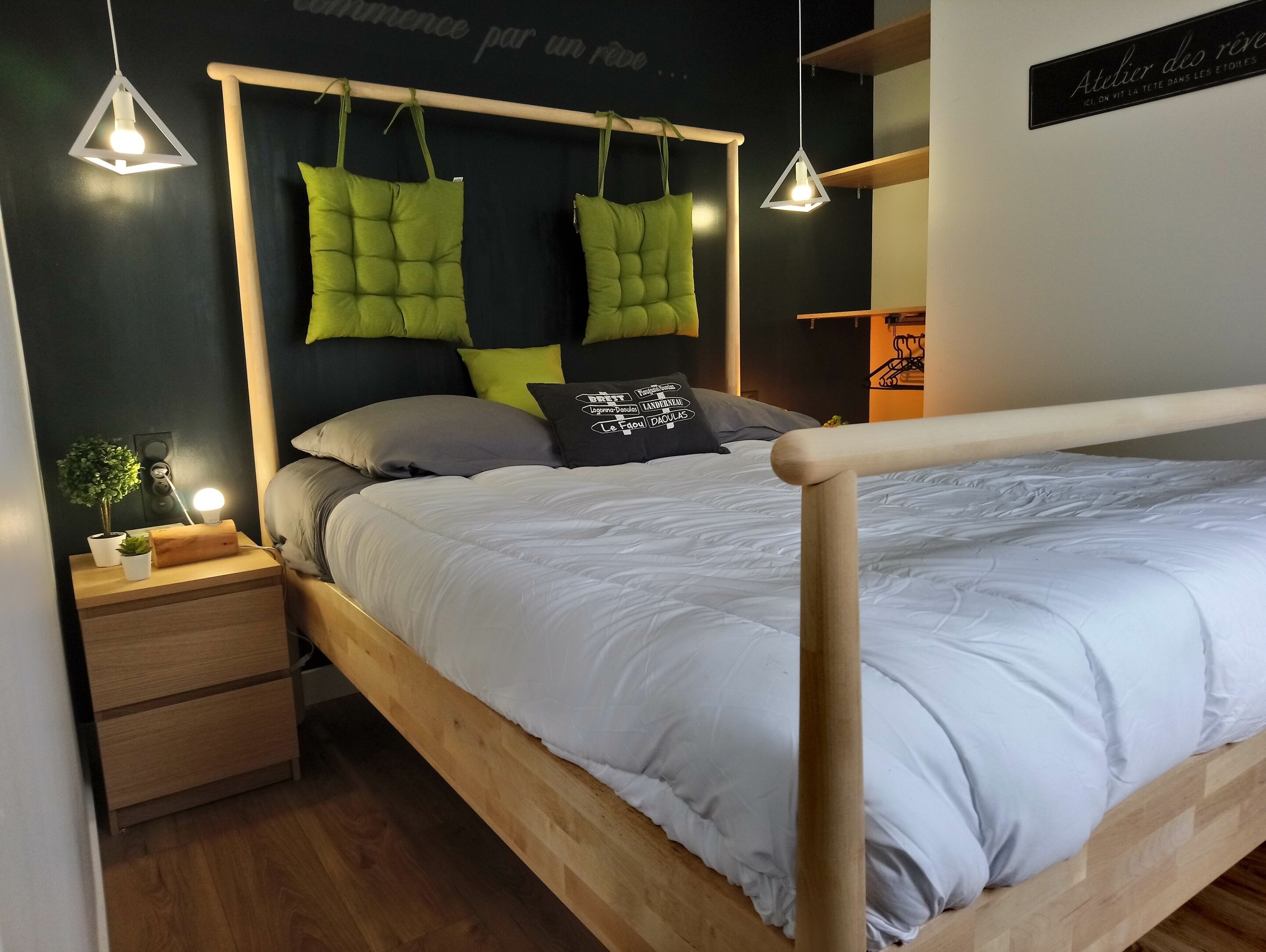 Un lit bien fait, avec un cadre en bois, une table de chevet avec une lampe et un mur orné d’une enseigne.