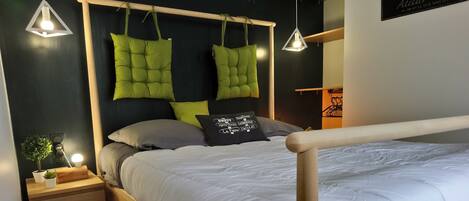 Un lit bien fait, avec un cadre en bois, une table de chevet avec une lampe et un mur orné d’une enseigne.