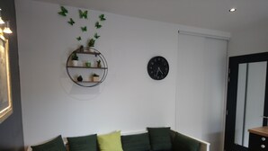A room with a bed, a wall clock, a shelf with plants, and a door.