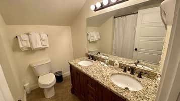 A bathroom with two sinks, a toilet, a mirror with lights, and a towel rack.