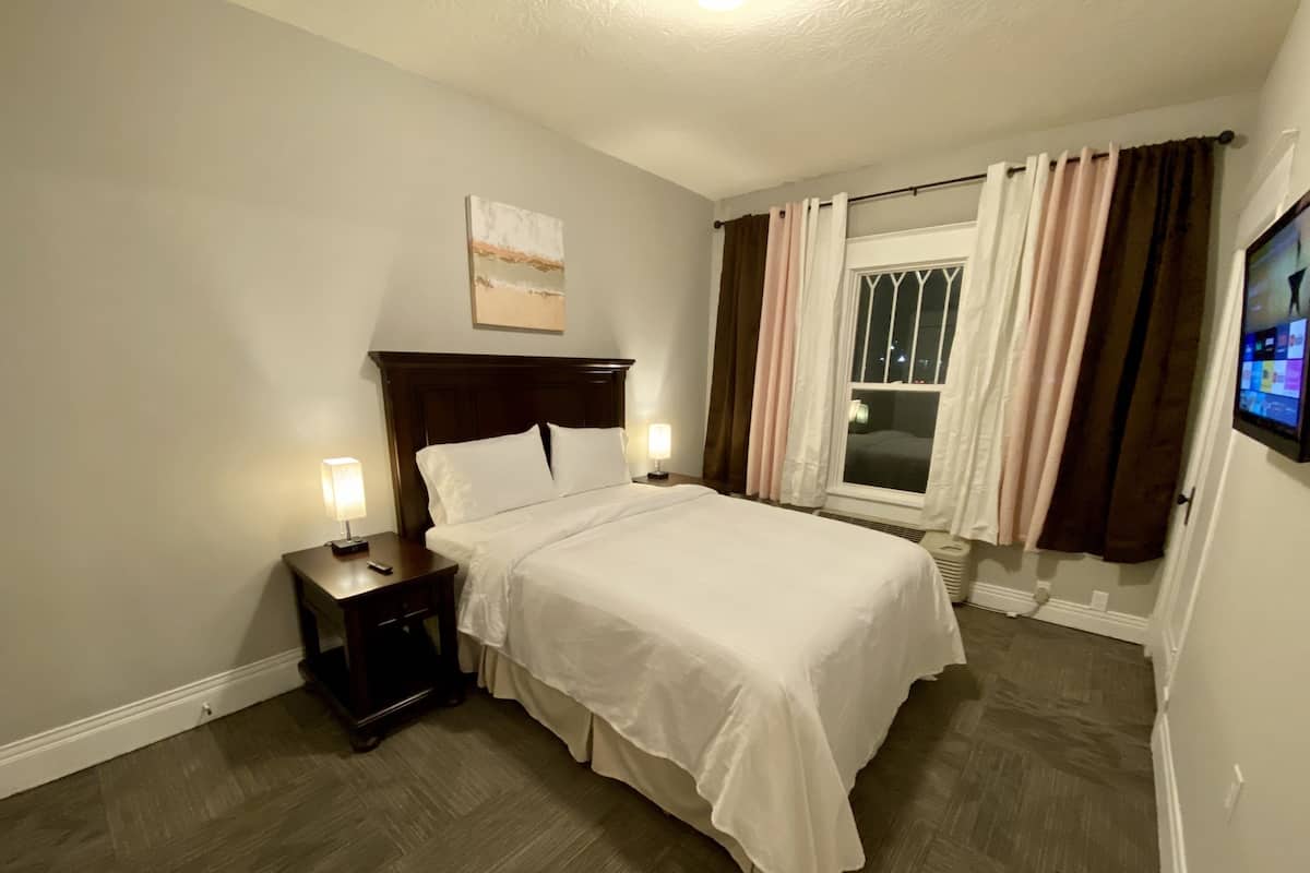 A neatly made bed with white linens, a wooden headboard, and two bedside lamps.