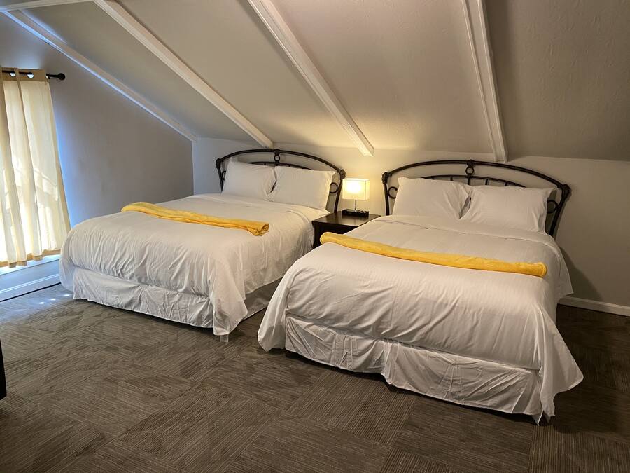 A hotel room with two beds, a nightstand with a lamp, and a window with curtains.