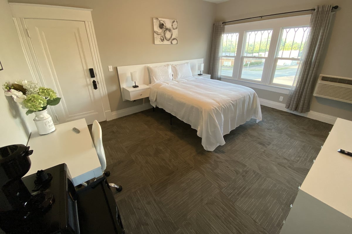 A bedroom with a bed, bedside table, nightstand, and a window with curtains.