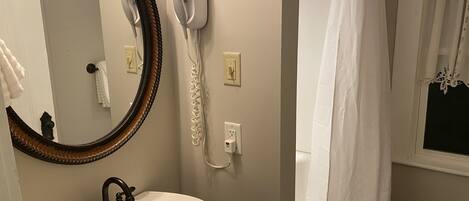 A bathroom with a white sink, a mirror with a wooden frame, a hairdryer, and a white shower curtain.