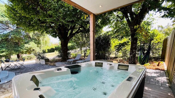 Un bain à remous doté d’une terrasse en bois et de chaises longues, le tout entouré d’arbres.