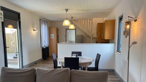 Un intérieur moderne avec un canapé, une table à manger et des chaises. On y trouve également un coin cuisine avec des placards et un plan de travail. Un escalier est visible au fond.