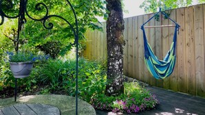 Un jardin avec un hamac, un arbre et des plantes en pot.