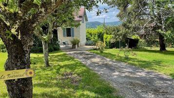 A rustic house with a gravel path leading to the entrance, surrounded by lush greenery and trees.
