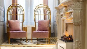 A room with two gold-framed chairs with pink cushions, a white fireplace with ornate details, and a patterned rug on the wooden floor. - President - romantic design apartment in the centre of Prague (Hlavní město Praha)
