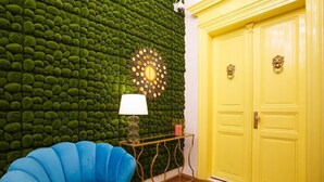 A room with a green textured wall, a blue chair, a gold lamp, a yellow door, and a small table with a lamp. - President - romantic design apartment in the centre of Prague (Hlavní město Praha)
