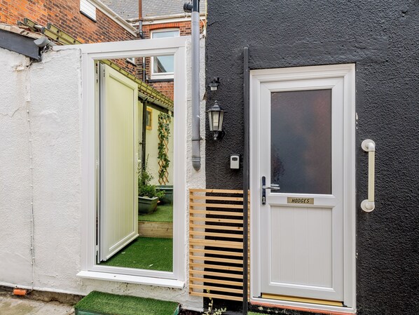 A property with a white door labeled 'HODGES,' a white exterior wall, and a small garden area visible through an open door.