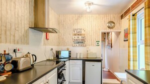 A compact kitchen with a toaster, kettle, and microwave on the counter, a small refrigerator, and a sink. There are wooden panel walls and a ceiling light fixture.