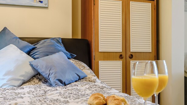 A neatly made bed with a floral-patterned bedspread, a plate of croissants, and two glasses of orange juice on a wooden tray.