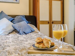 A neatly made bed with a floral-patterned bedspread, a plate of croissants, and two glasses of orange juice on a wooden tray.