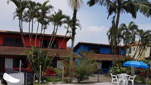 Una piscina con suelo de baldosas, rodeada de palmeras y un edificio rojo con techo de tejas.
