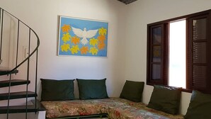 Una habitación con techo de madera, una cama con ropa de cama floral, un cuadro de una paloma y una ventana con marco de madera.