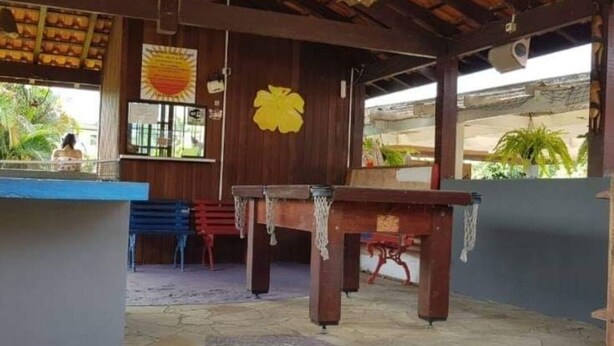 Un espacio al aire libre techado con una mesa y sillas de madera, una barra azul y una decoración floral amarilla en la pared.