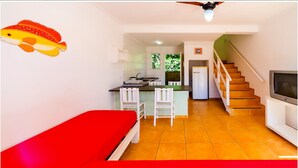 Un espacio habitable compacto con kitchenette, zona de comedor, televisor y escalera.