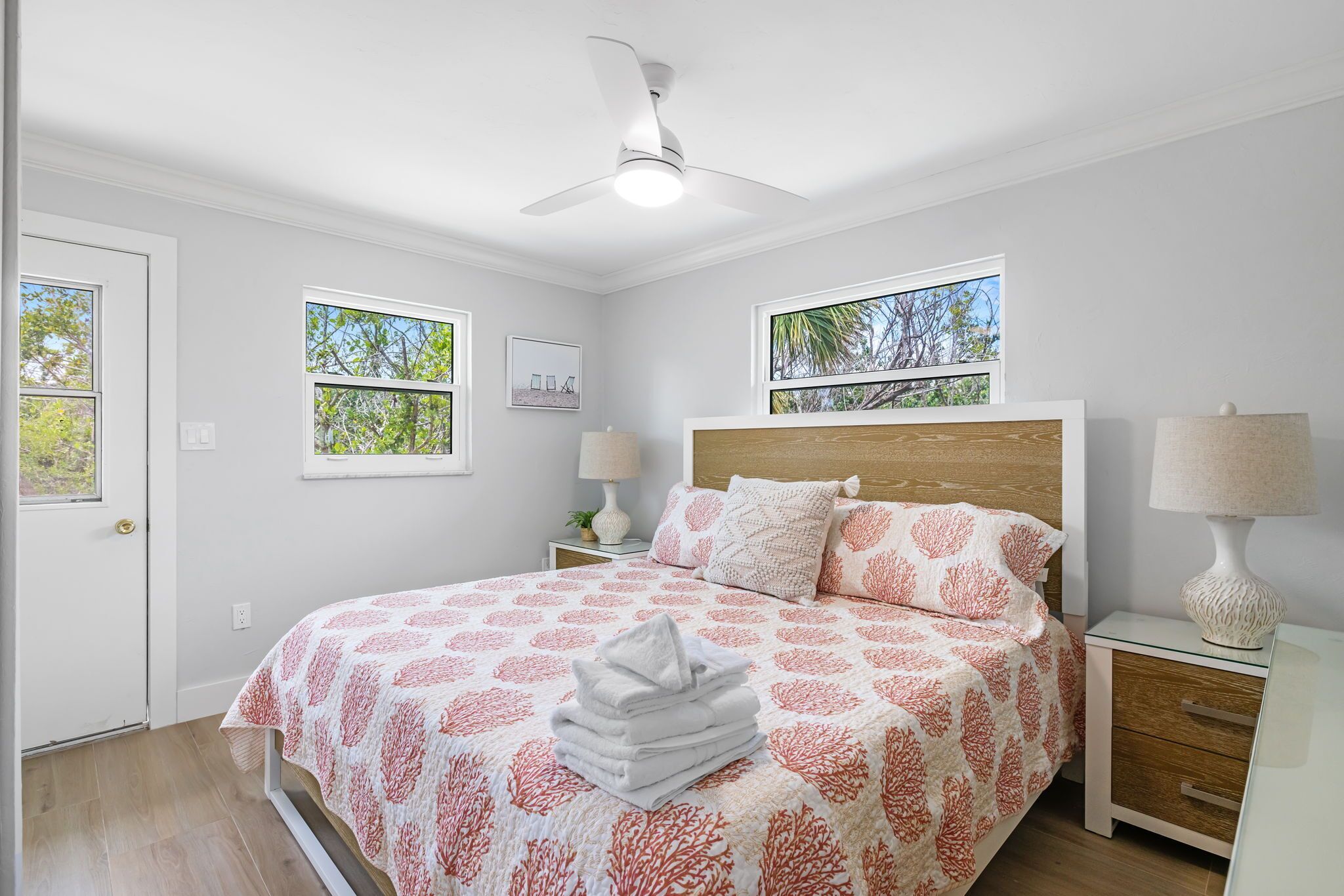 A bedroom with a bed, two bedside tables, a ceiling fan, and two windows.