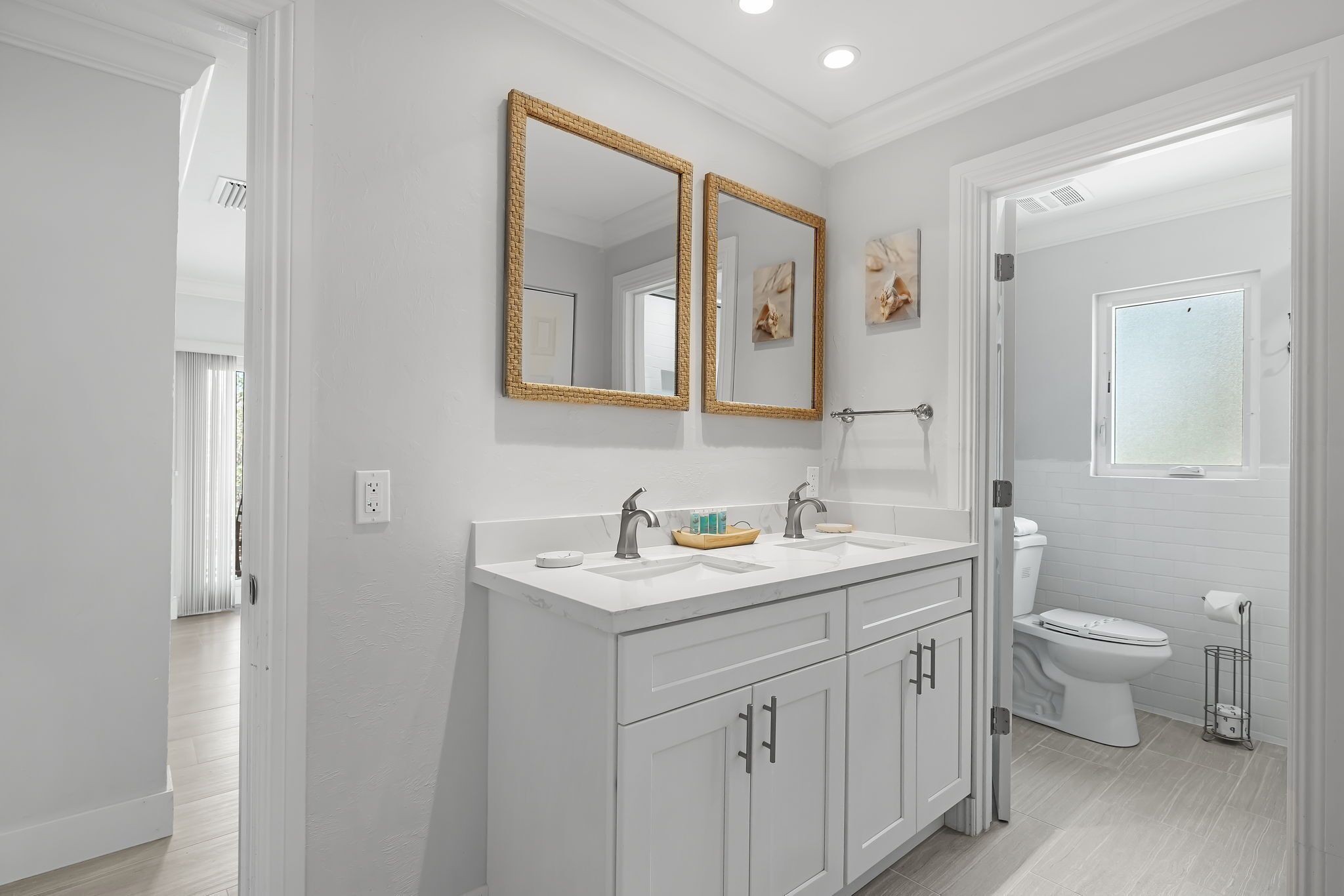 A modern bathroom with white cabinetry, a double vanity, a toilet, and a shower area.
