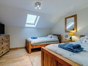 A bedroom with a skylight, wooden furniture, a bed with a blue blanket, a bedside table with a lamp, and a mirror.