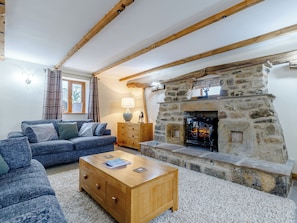 A cozy living room with a stone fireplace, wooden beams, a blue sofa, and a wooden coffee table.