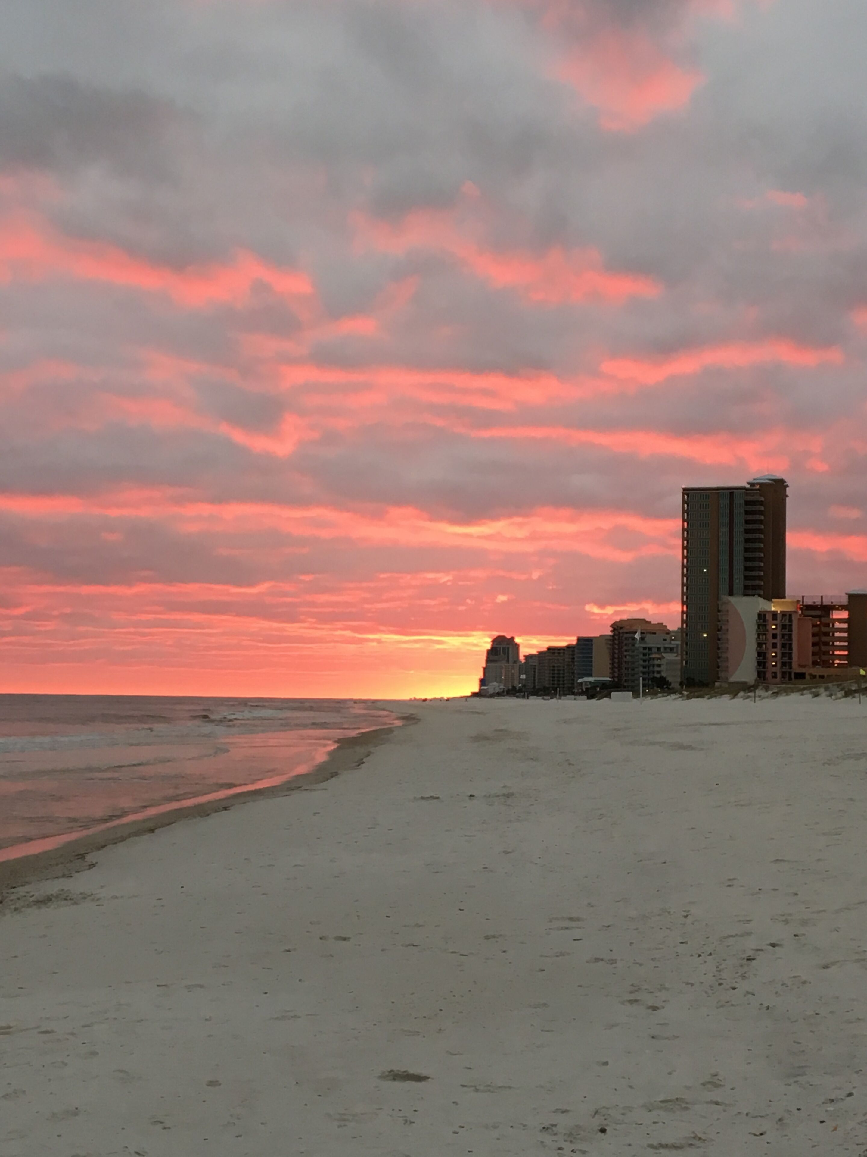 Una playa con atardecer, edificios al fondo y cielo despejado.