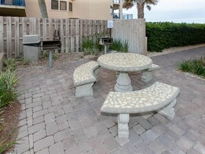 Un espace patio avec une table et des bancs en mosaïque, une clôture en bois et une poubelle.