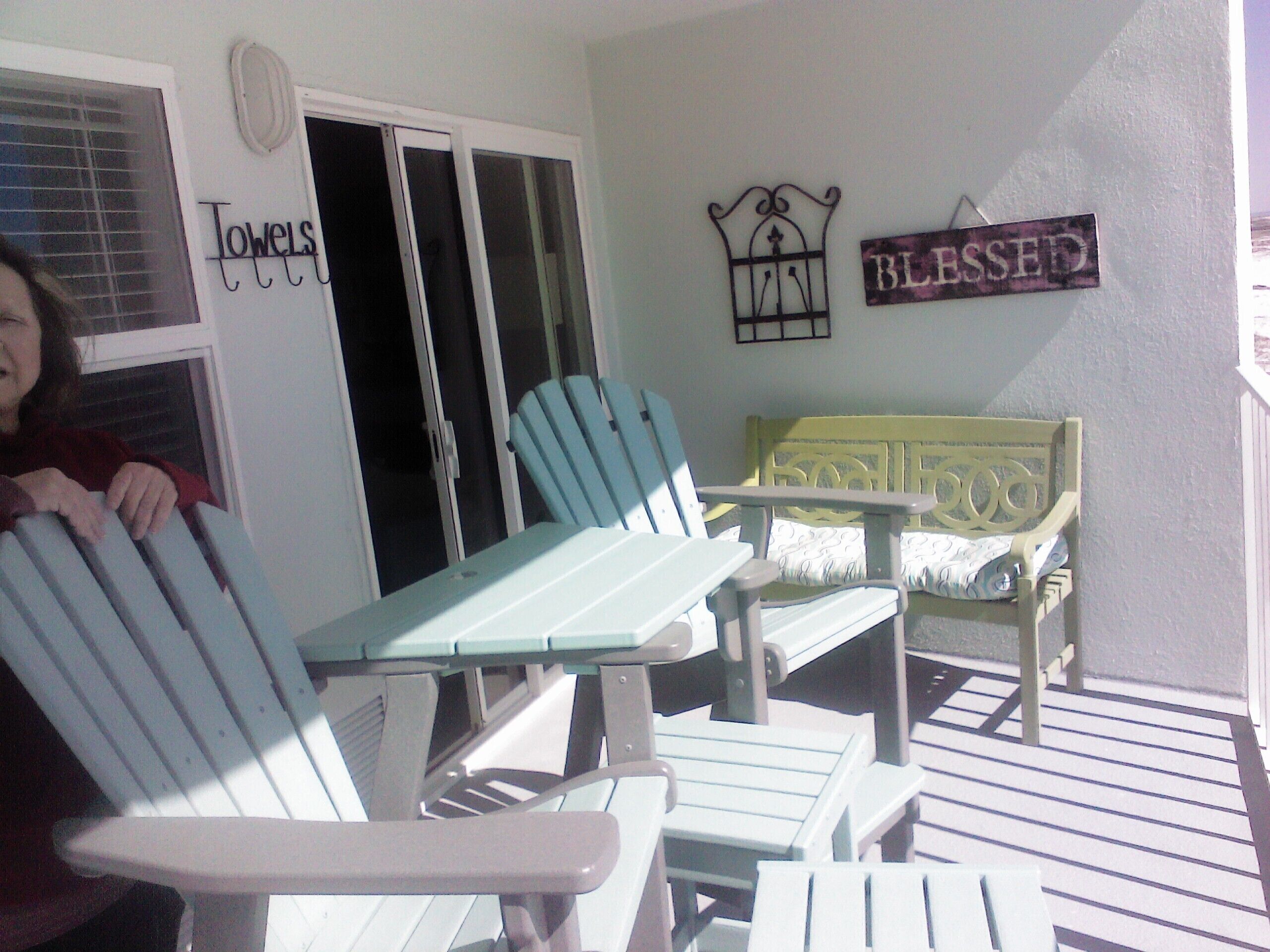 A porch with Adirondack chairs and a bench, a door with a towel sign, and a 'Blessed' sign on the wall.