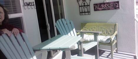 A porch with Adirondack chairs and a bench, a door with a towel sign, and a 'Blessed' sign on the wall.