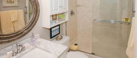 A bathroom with a marble sink, a toilet, a glass shower enclosure, and a cabinet labeled "First Aid".