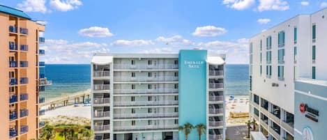 A multi-story hotel with a pool, beachfront view, and several balconies.