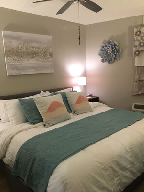 Une chambre à coucher comprenant un lit, un ventilateur de plafond, une lampe fixée au mur et un élément décoratif mural.
