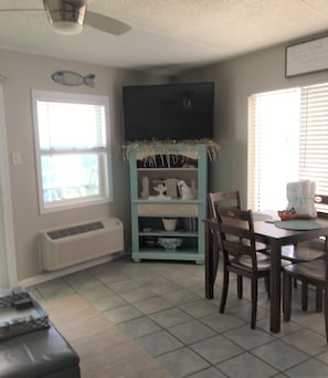 A dining area with a table and chairs, a teal cabinet with decorative items, a ceiling fan, and a window with blinds.