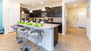 A modern kitchen with dark cabinets, a large island with bar stools, stainless steel appliances, and pendant lighting.